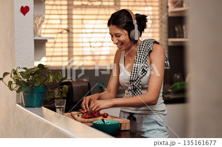 Music headphones, morning and woman cooking breakfast of healthy strawberry food at home. Kitchen, headphone and happy female person making snack with fruits while listening to audio, sound and radio 135161677