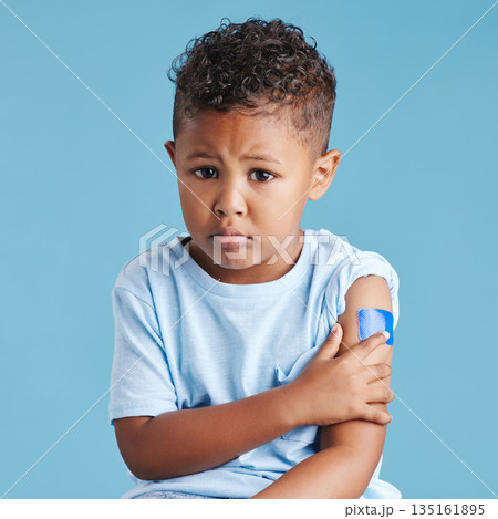 Portrait, sad and kid with arm bandage in studio isolated on a blue background. Face, upset and child with plaster after vaccine, injury or wound for healthcare wellness, first aid or medical help. 135161895