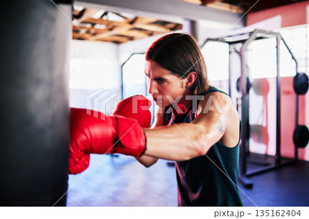 Punching bag, man and boxing in gym for exercise, workout or training for fight. Boxer, sports and serious fitness athlete punch for challenge, competition or exercising body for martial arts power. 135162404