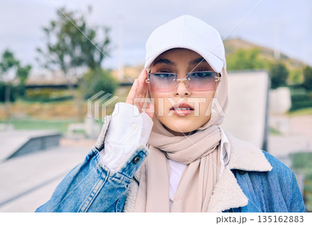 Portrait, fashion or sunglasses with an islamic woman outdoor in a cap and scarf for contemporary style. Muslim, faith or hijab with a trendy young arab female person posing outside in modern eyewear 135162883