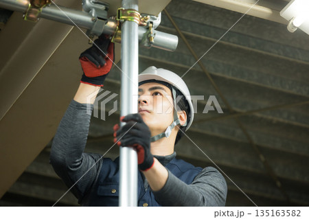 工場現場で単管パイプを組む作業員 工場現場で単管パイプを組む作業員 135163582