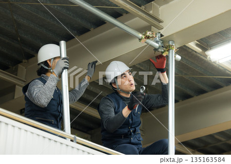 工場現場で単管パイプを組む作業員 工場現場で単管パイプを組む作業員 135163584