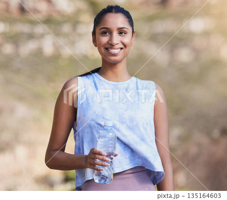 Fitness, water and woman running in nature for race training by an outdoor mountain for health. Sports, exercise and female athlete with a bottle of liquid for hydration during a cardio workout. 135164603