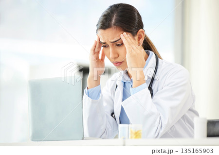 Mental health, woman doctor with headache and laptop at her desk in a modern office. Anxiety or stress, depression or mistake and sad female surgeon or nurse at her workstation with problem at work 135165903
