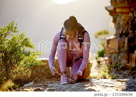 Hiking, shoelace and woman on mountain outdoor with a backpack for adventure and fitness workout. Black athlete person tying shoes for training, exercise or trekking in nature for wellness and travel Hiking, shoelace and woman on mountain outdoor with a backpack for adventure and fitness workout. Black athlete person tying shoes for training, exercise or trekking in nature for wellness and travel 135166656
