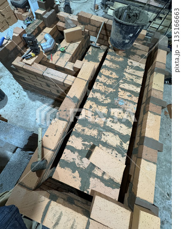 Fresh brickwork of a heating stove ash pit and bench. Overlap of the benchs smoke channels. Fresh brickwork of a heating stove ash pit and bench. Overlap of the benchs smoke channels. 135166663