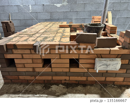 Fresh brickwork of a heating stove with a bench. Cleaning access channels and a metal pipe for convection heating are visible. 135166667