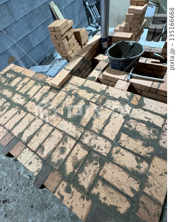 Fresh brickwork of a heating stove with a bench. Metal pipe for convection heating. Oblique Angle.  135166668