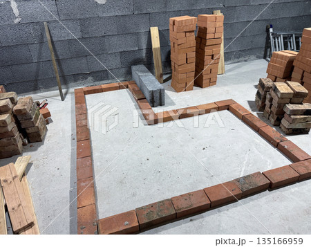 Contour of a heating stove with a bench. Laid out of brick on a concrete screed. Bricks and tools nearby. 135166959