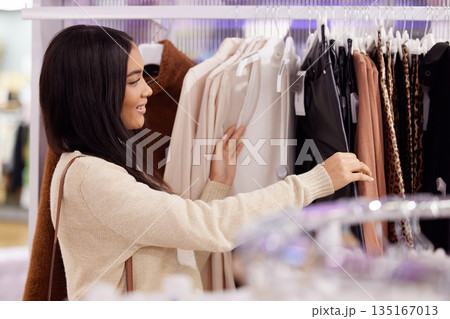 Shopping, retail and woman with clothes in store for sale, discount and bargain for clothing. Fashion boutique, mall and happy female person browse clothing rack for purchase, buying and promotion 135167013