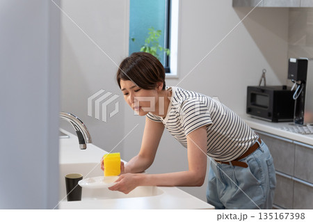 キッチンで皿洗いをする体調不良の女性 キッチンで皿洗いをする体調不良の女性 135167398