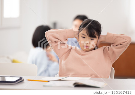 テーブルに広げた教科書を前に頭を抱える小学生の女の子 テーブルに広げた教科書を前に頭を抱える小学生の女の子 135167413