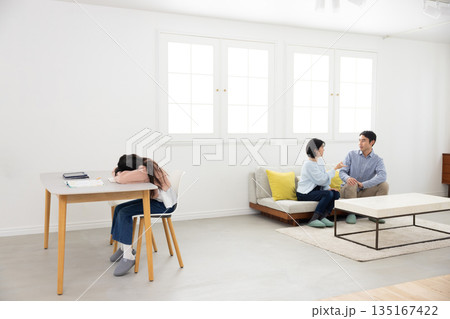 口論する両親の近くでテーブルに顔を伏せる小学生の女の子 135167422