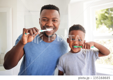 Portrait of a dad brushing his teeth with his child for dental care, health and wellness in the bathroom. Oral hygiene, teaching and young father doing morning mouth routine with his boy kid at home. Portrait of a dad brushing his teeth with his child for dental care, health and wellness in the bathroom. Oral hygiene, teaching and young father doing morning mouth routine with his boy kid at home. 135168685