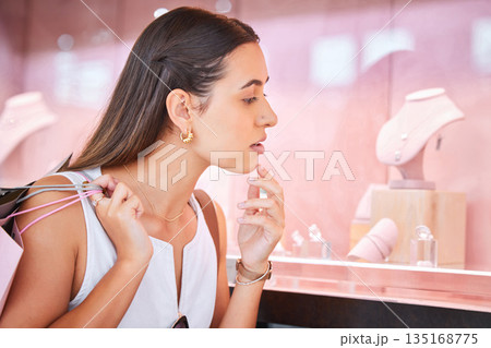 Window, jewelry store and a woman with a shopping bag in mall for fashion, sale or discount deal. Female person or customer thinking of product at retail shop with diamonds, jewellery and promotion Window, jewelry store and a woman with a shopping bag in mall for fashion, sale or discount deal. Female person or customer thinking of product at retail shop with diamonds, jewellery and promotion 135168775
