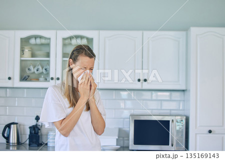Allergies, toilet paper and woman blowing her nose in the kitchen for a cold, flu or sneeze at her home. Illness, virus and young female person with tissue for sinus, hay fever or covid in apartment. 135169143