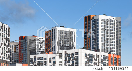 Cluster of highrise residential towers with modern facades in white, grey, and orange tones against 135169332