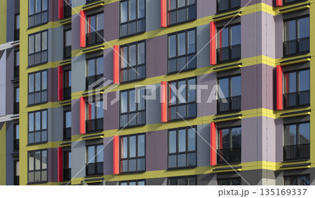 Colorful apartment building facade with bold yellow horizontal stripes and red window accents, 135169337