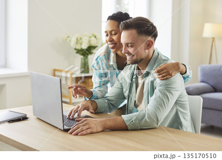 Smiling couple using laptop together at home table, planning finances online 135170510
