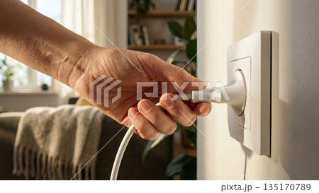 Close up of hand inserting electrical plug into wall socket. 135170789