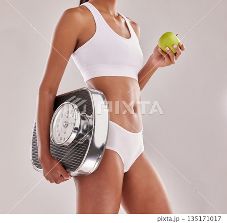 Woman in underwear, body and apple with scale and lose weight, health with fitness and nutrition on studio background. Female model, healthy food and fruit with diet, detox and vegan lifestyle Woman in underwear, body and apple with scale and lose weight, health with fitness and nutrition on studio background. Female model, healthy food and fruit with diet, detox and vegan lifestyle 135171017