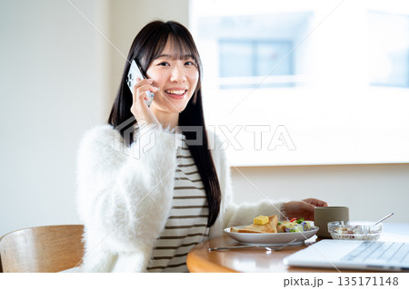 朝食をとりながらスマホで通話する女性 135171148