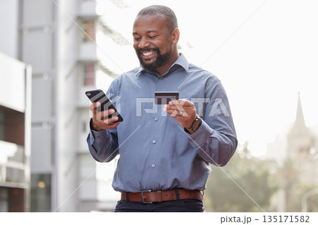 Ecommerce, businessman with smartphone and credit card outside in the city happy. Online shopping, happiness with African male person with a cellphone and his bank information in urban street Ecommerce, businessman with smartphone and credit card outside in the city happy. Online shopping, happiness with African male person with a cellphone and his bank information in urban street 135171582