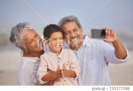 Selfie, happy and grandparents with child at beach for vacation, bonding and generations. Picture, travel and young boy with senior man and woman in nature for smile, happiness and technology Selfie, happy and grandparents with child at beach for vacation, bonding and generations. Picture, travel and young boy with senior man and woman in nature for smile, happiness and technology 135171586
