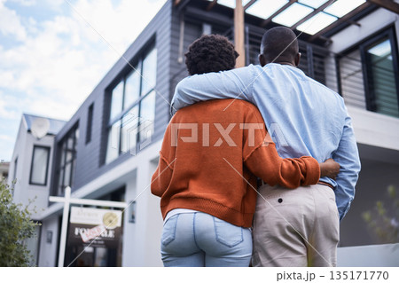 Love, hugging and back of couple by their new home, property or real estate standing together. Relocation, romance and behind of an African man and woman homeowners embracing by their modern house. 135171770