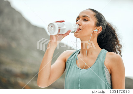Break, fitness and a woman with water in nature and music for exercise, cardio and rest from running. Sports, streaming audio and a young athlete with a bottle for a drink after training at a park 135172056