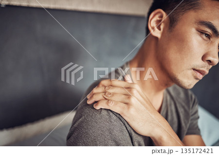 Stress, sick and man with shoulder pain in his bedroom in recovery from an accident or injury. Illness, medical emergency and male person holding a sprain back muscle while resting in his apartment. 135172421