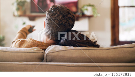 Watching tv, couple and love in a home on a living room sofa with bonding feeling relax. Cuddle, lounge couch and house with a television and movie with people back streaming series with remote 135172935