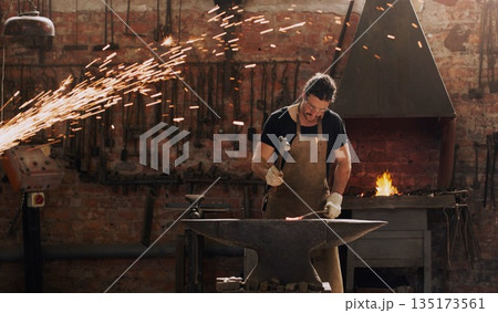 Hammer, anvil and fire with a man working in a factory for metal work manufacturing or production. Industry, welding and trade with a male blacksmith at work in a forge, plant or industrial workshop Hammer, anvil and fire with a man working in a factory for metal work manufacturing or production. Industry, welding and trade with a male blacksmith at work in a forge, plant or industrial workshop 135173561