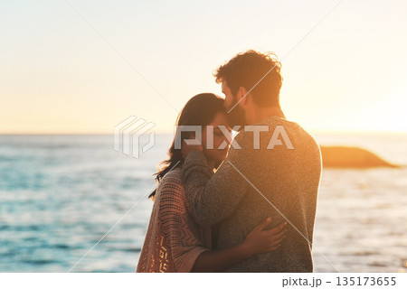 Sunset, beach and couple kiss forehead for relax, bonding and quality time on romantic date. Nature, travel and man and woman embrace for anniversary or honeymoon on holiday, weekend and vacation 135173655