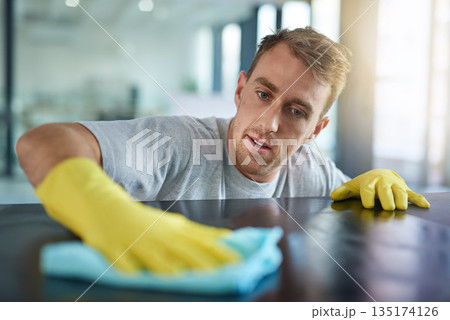 Man with gloves, office cleaning service and janitor dusting dirt for health and hygiene in workplace. Professional cleaner wiping table in workspace, maintenance and disinfectant on cloth for germs. 135174126