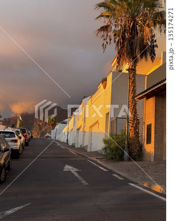 Warm evening sunlight reflecting on colorful building walls and palm trees along a quiet street in Tenerife. 135174271