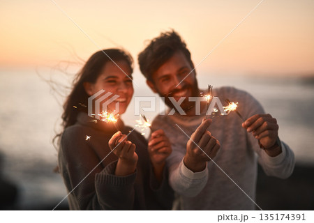 Happy, beach and couple with sparklers for celebration and party with sparks on romantic date. Love, sunset and excited man and woman with fireworks for honeymoon on holiday, weekend and vacation Happy, beach and couple with sparklers for celebration and party with sparks on romantic date. Love, sunset and excited man and woman with fireworks for honeymoon on holiday, weekend and vacation 135174391