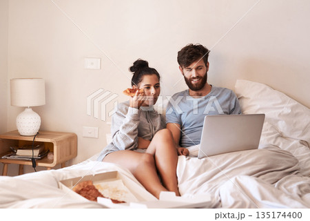 Couple, pizza and movie on laptop in bed with junk food and streaming series. Eating, computer video and meal in a bedroom at home with man and woman together with bonding and online watching 135174400