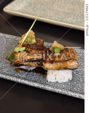 Elegant Japanese dish of unagi nigiri sushi garnished with herbs and sauce, served on a modern slate plate. Elegant Japanese dish of unagi nigiri sushi garnished with herbs and sauce, served on a modern slate plate. 135174603