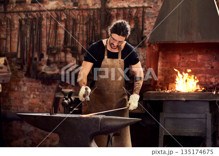 Worker, blacksmith and metal forge in workshop and manual working on hot steel with hammer, fire and sparks. Man, welding job or iron tools manufacturing and expert, trade and dark workspace Worker, blacksmith and metal forge in workshop and manual working on hot steel with hammer, fire and sparks. Man, welding job or iron tools manufacturing and expert, trade and dark workspace 135174675