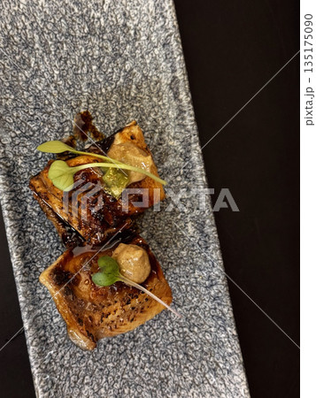 Two seared gourmet cubes, possibly tofu or fish, garnished with microgreens and sauce, served on a gray stone plate. Two seared gourmet cubes, possibly tofu or fish, garnished with microgreens and sauce, served on a gray stone plate. 135175090