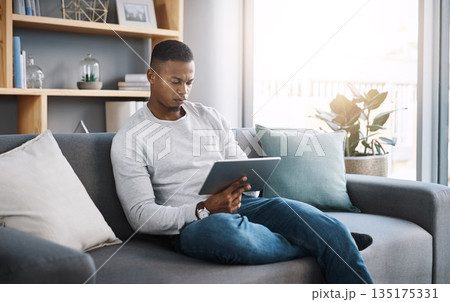 Remote work, tablet and man on sofa reading email, social media post or streaming video on subscription service. Search, scroll and internet, freelance worker checking website on couch in living room Remote work, tablet and man on sofa reading email, social media post or streaming video on subscription service. Search, scroll and internet, freelance worker checking website on couch in living room 135175331