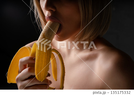 Woman enjoying a banana in a sensual pose under soft lighting 135175332