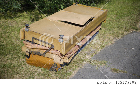 A wooden cart rests on the grass close to a path in a green area. The cart shows signs of wear, with some parts missing or damaged in the sunlight A wooden cart rests on the grass close to a path in a green area. The cart shows signs of wear, with some parts missing or damaged in the sunlight 135175508