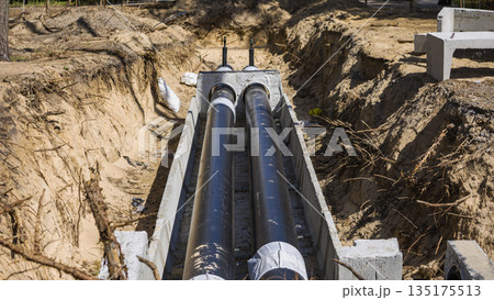 New pipelines are installed in a trench at a construction site. Workers have dug out sections of ground to place the pipes securely in the soil New pipelines are installed in a trench at a construction site. Workers have dug out sections of ground to place the pipes securely in the soil 135175513