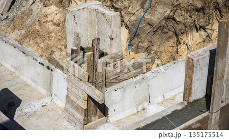Workers build a concrete foundation with wooden frames at a construction site on a sunny day. Tools and materials are visible around the area Workers build a concrete foundation with wooden frames at a construction site on a sunny day. Tools and materials are visible around the area 135175514
