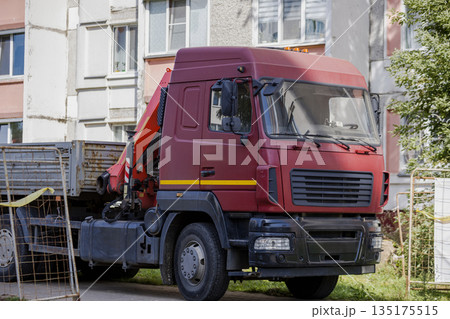 A red truck is parked next to a residential building with a crane on the back. The scene shows a blue sky and several windows in the background A red truck is parked next to a residential building with a crane on the back. The scene shows a blue sky and several windows in the background 135175515