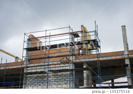 Workers are building a structure with brick walls and scaffolding. The sky is overcast, indicating a chance of rain at the construction site Workers are building a structure with brick walls and scaffolding. The sky is overcast, indicating a chance of rain at the construction site 135175518