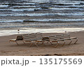Empty beach chairs on Jurmala shore with waves crashing under cloudy sky 135175569