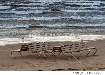Empty beach chairs on Jurmala shore with waves crashing under cloudy sky 135175569